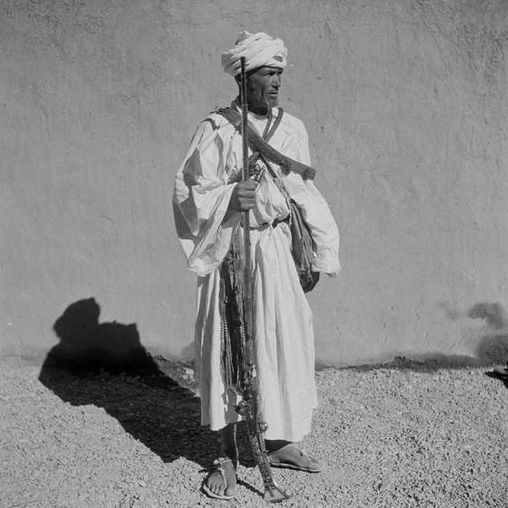 Agdz/ Guerrier en tenue traditionnelle de la haute vallée avec son fusil, moukala, ses sacs à poudre, son poignard, sa choukara, sa ceinture à balles passée en bandoulière.