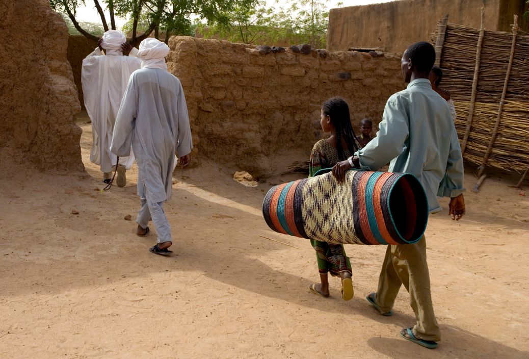 NIGER. Tajae. Tuareg slave Youssouff carries mat for Tuareg chieftan Ibrahim Agali (l) as he leaves palace with his cousin Sayadi Ibrahim (r). 2005.